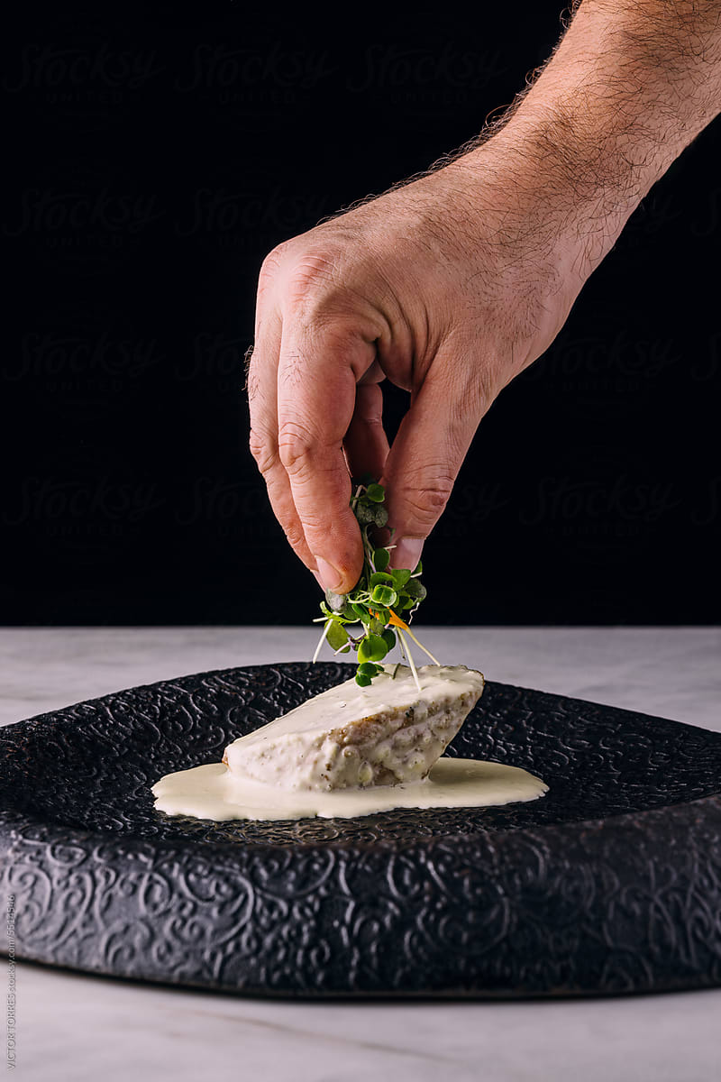 Crop chef decorating fish slice with herbs
