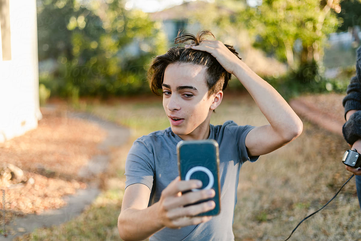 Teen boy looking at his phone before haircut outdoor