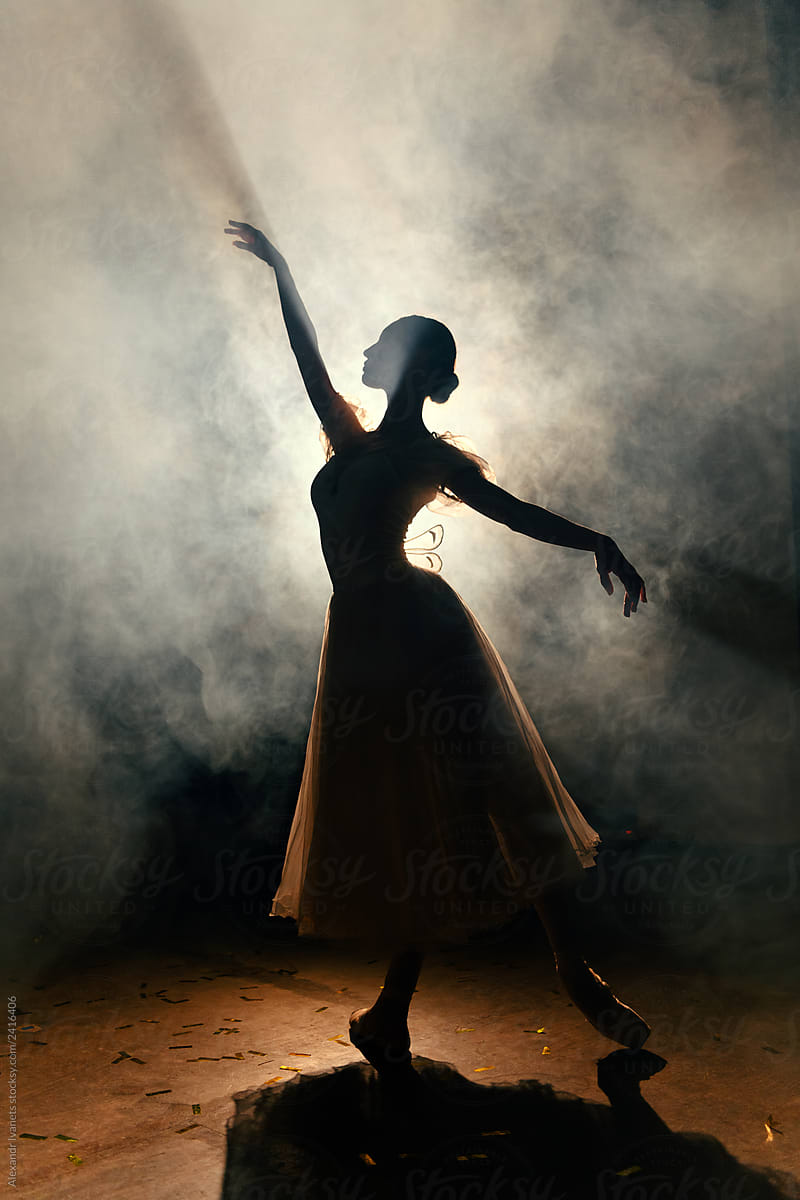 Ballerina in dress stretching on scene in darkness