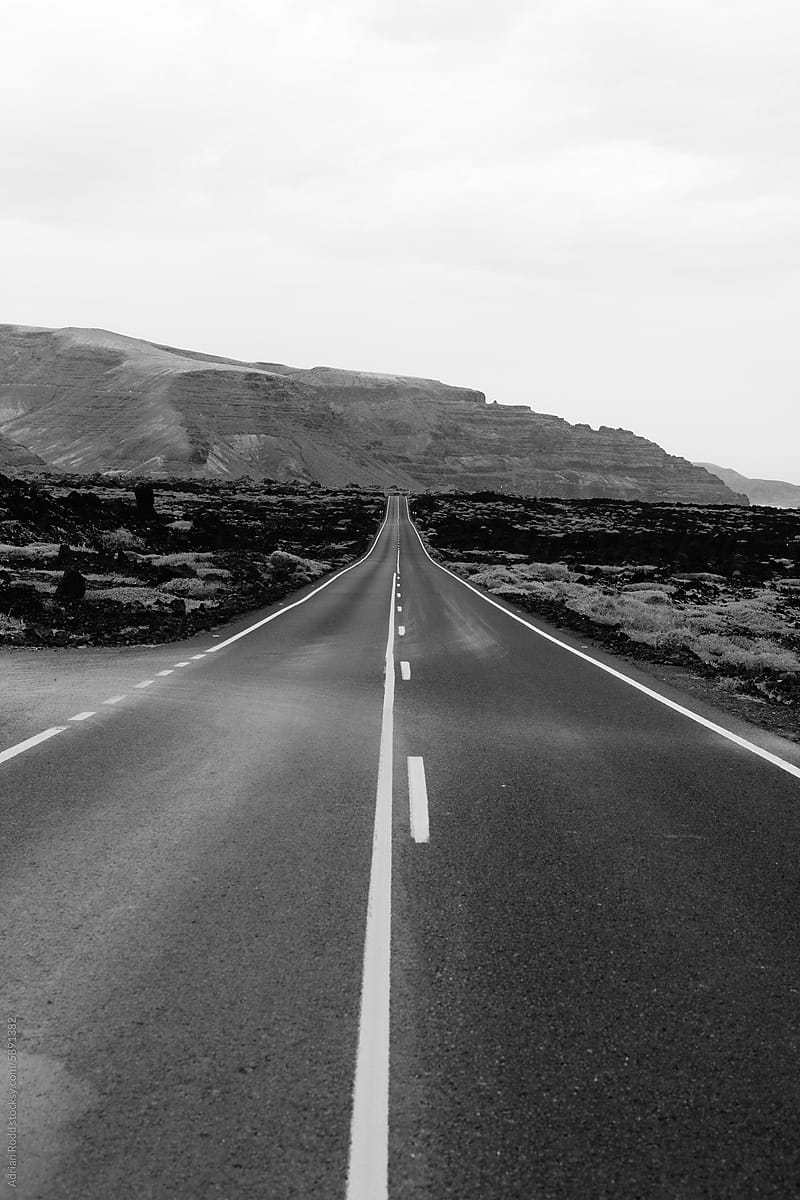 A monochromatic photograph depicts a highway cutting through a desert