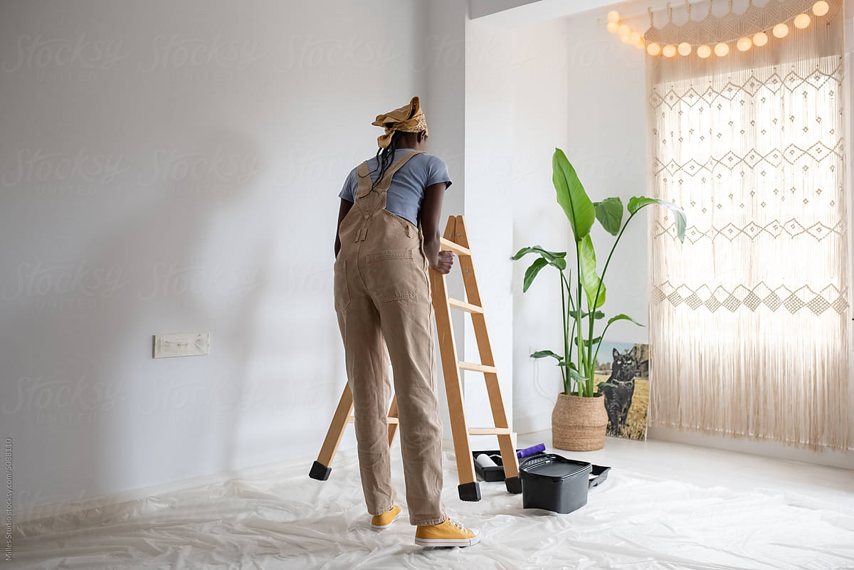 Black painter putting ladder near wall