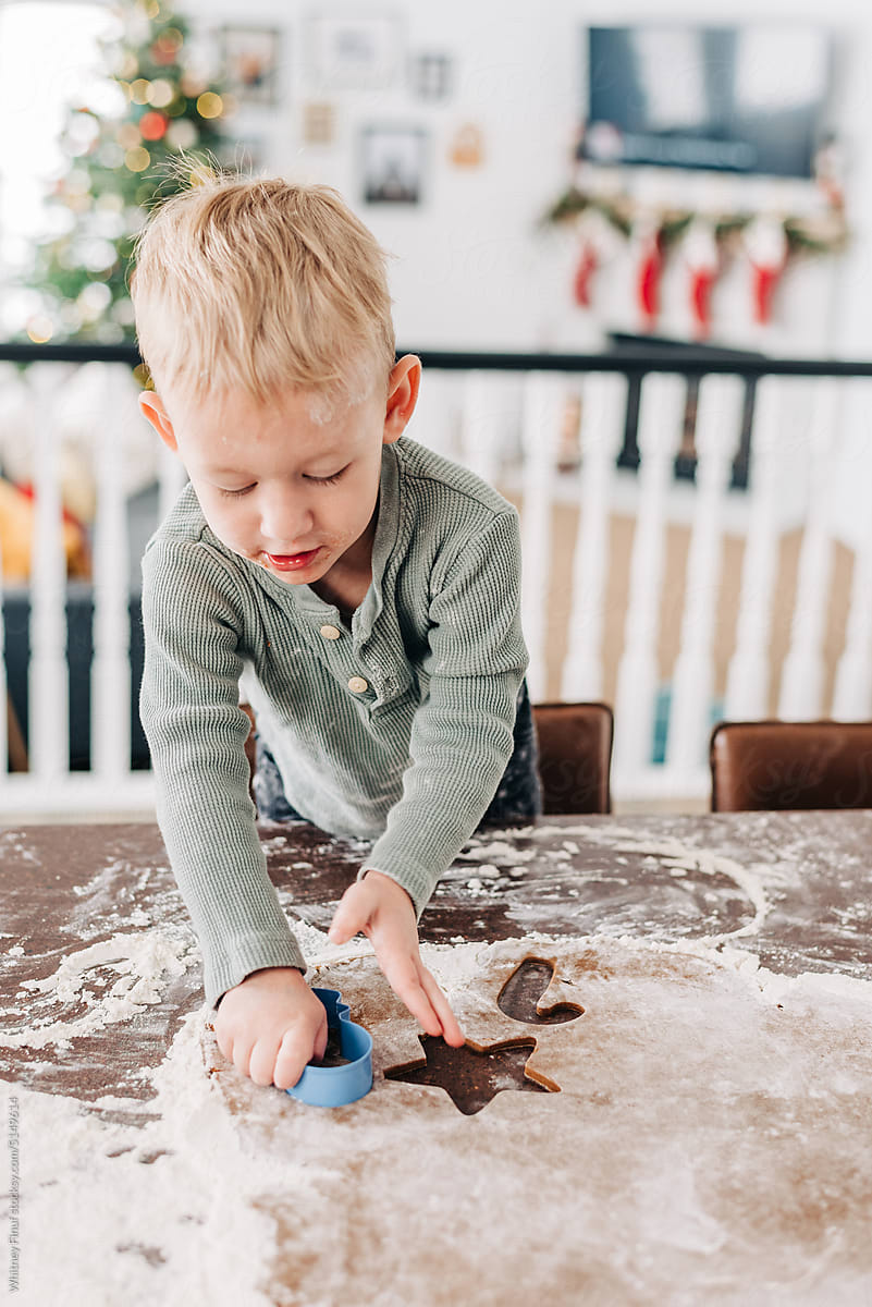 A two year old toddler cuts a gingerbread cookie with a cookie cutter