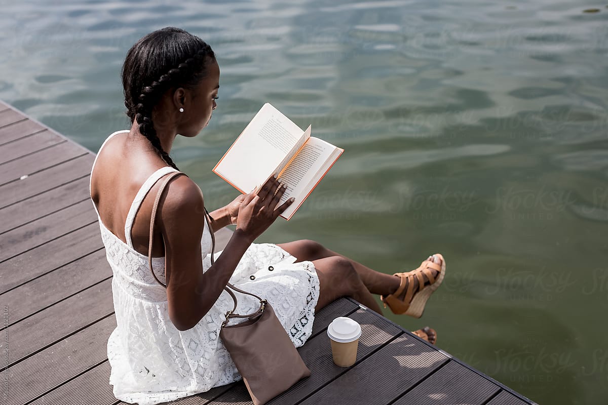 A woman reading a book along a river