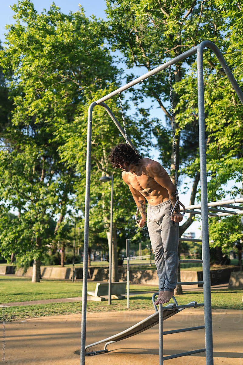 A man doing pull-ups at the rings in a park