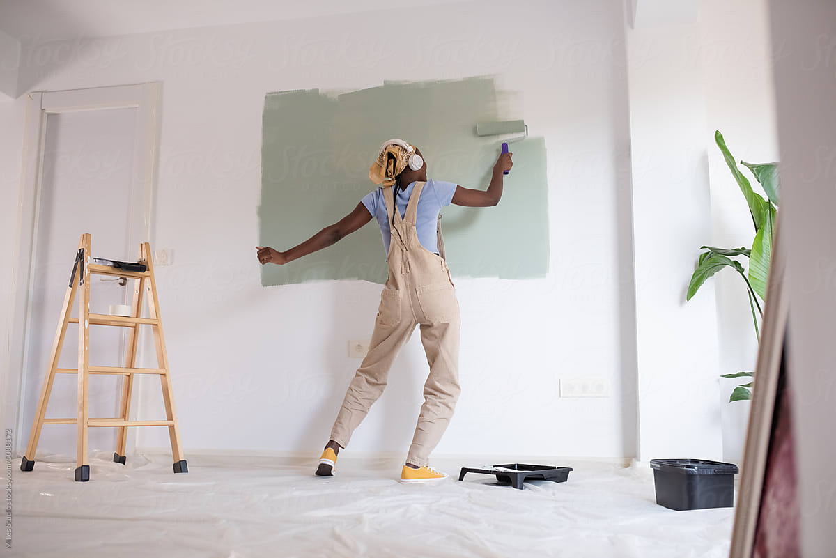 Energetic black woman painting wall with roller