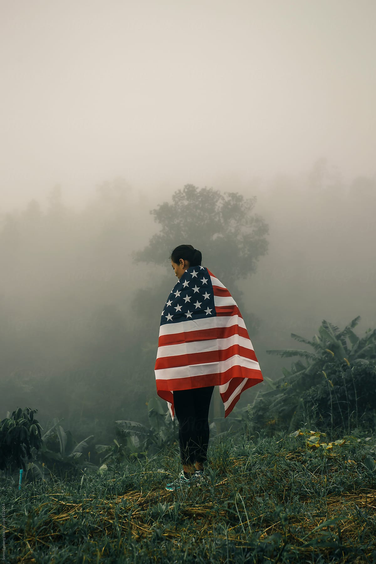 Ethnic woman carrying american flag in foggy landscape