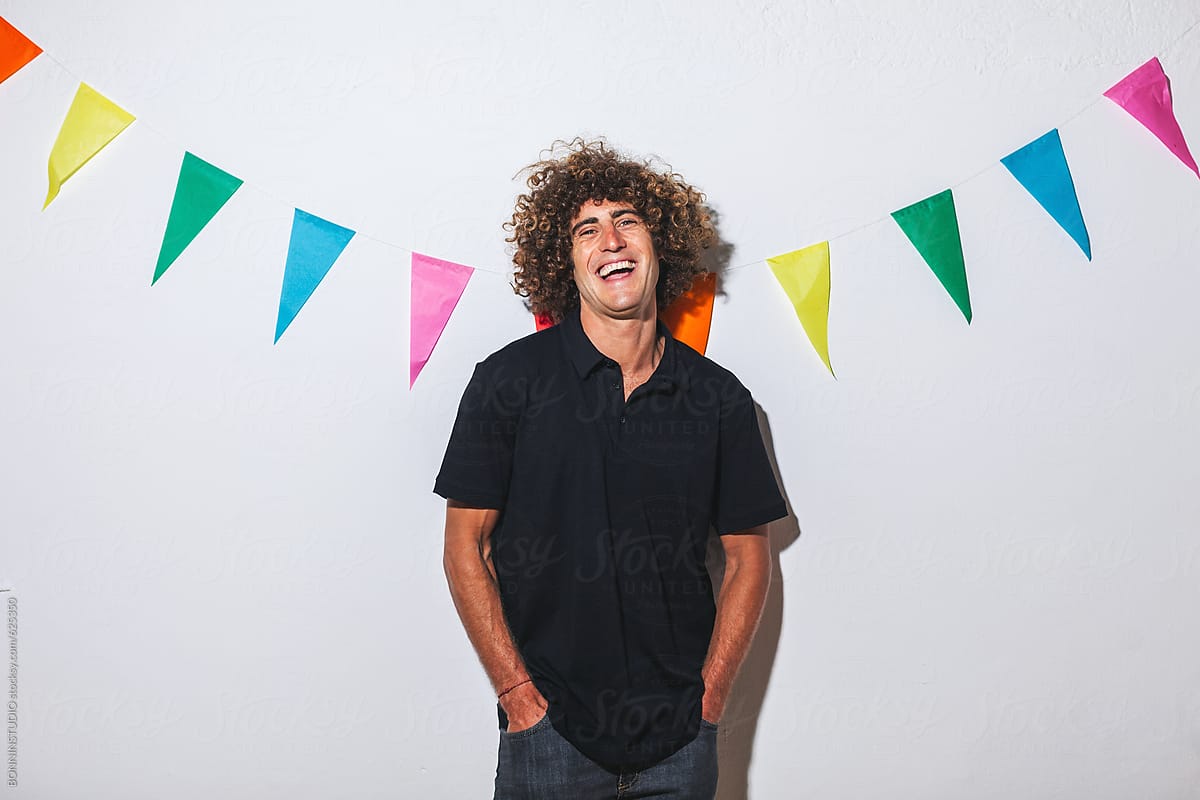 Portrait of a laughing caucasian man with afro hairstyle standing in front of a colourful banner.