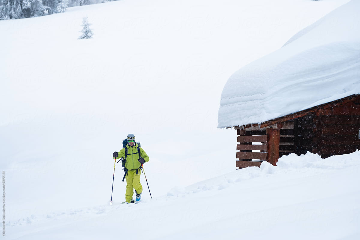 A man ski touring near old vintage house with deep snow.