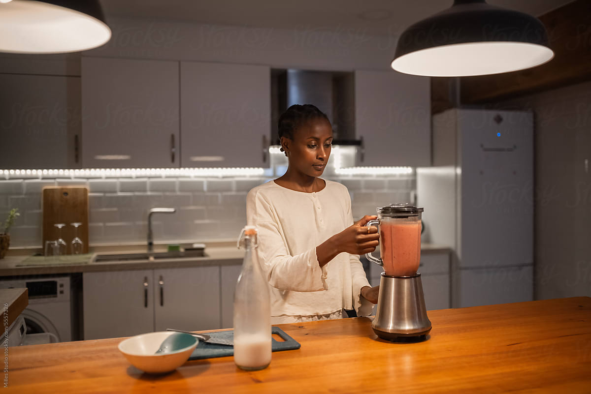 Woman preparing smoothie for dinner at countertop