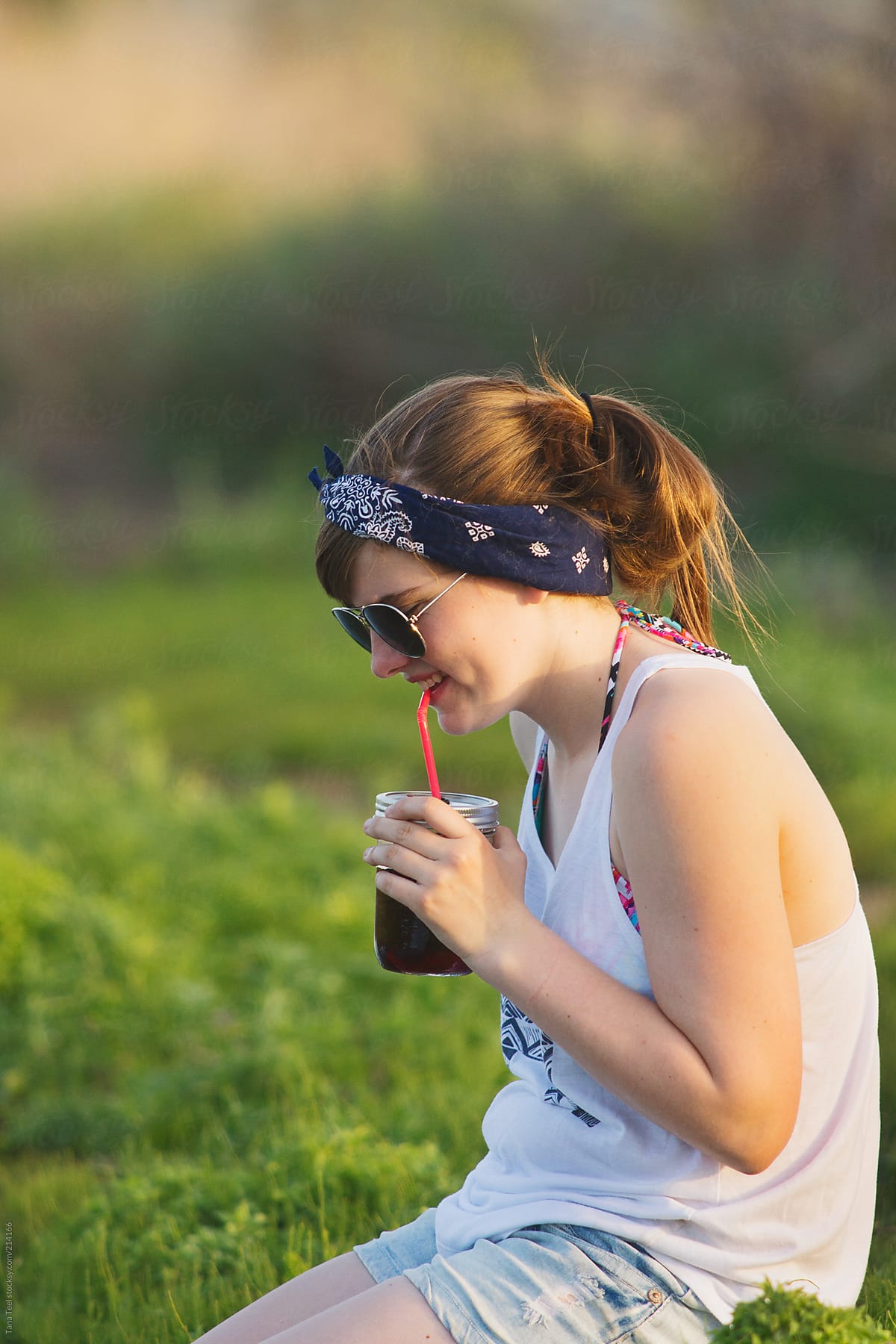Teen girl sipping her drink from a straw in a jar on a summer day