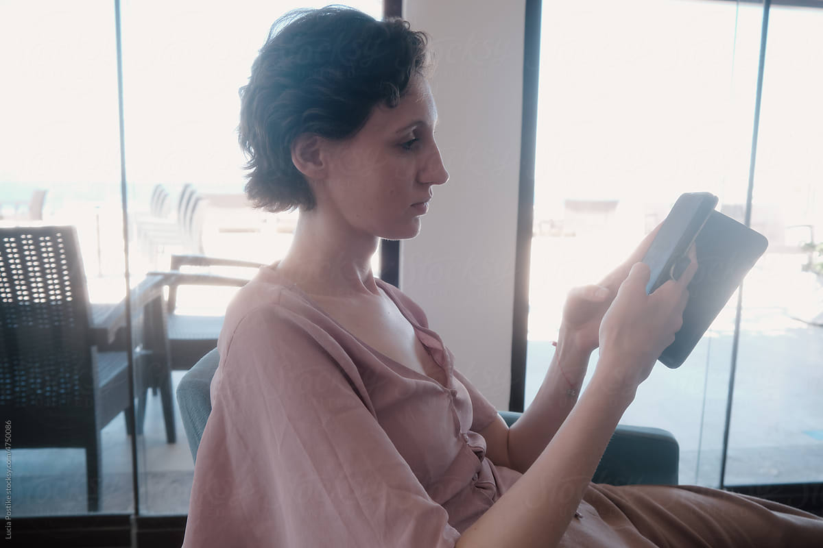 A woman in a pink blouse sits in a cafe and looks at the phone.