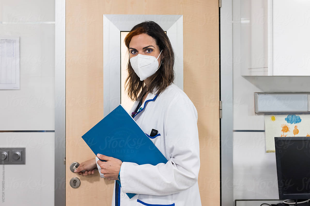 Doctor with a mask holding blue folder and opening a door at the laboratory