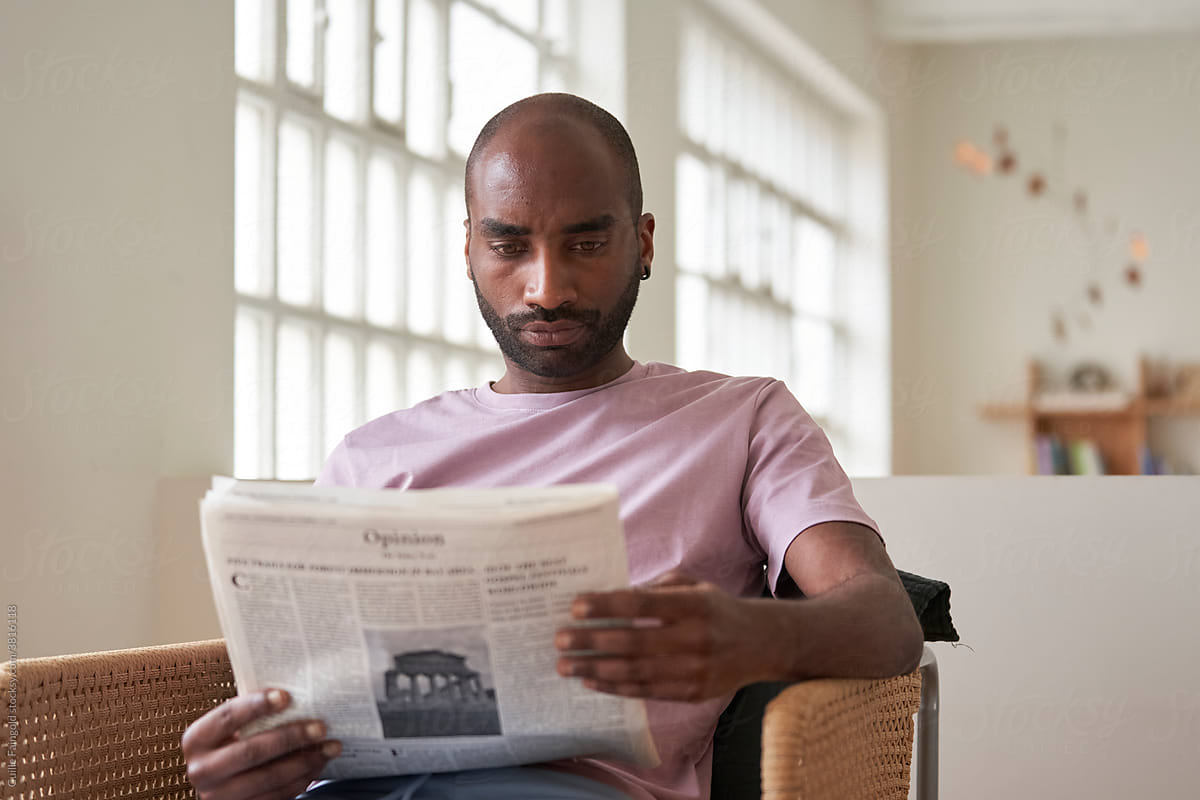 Focused black man reading newspaper at home
