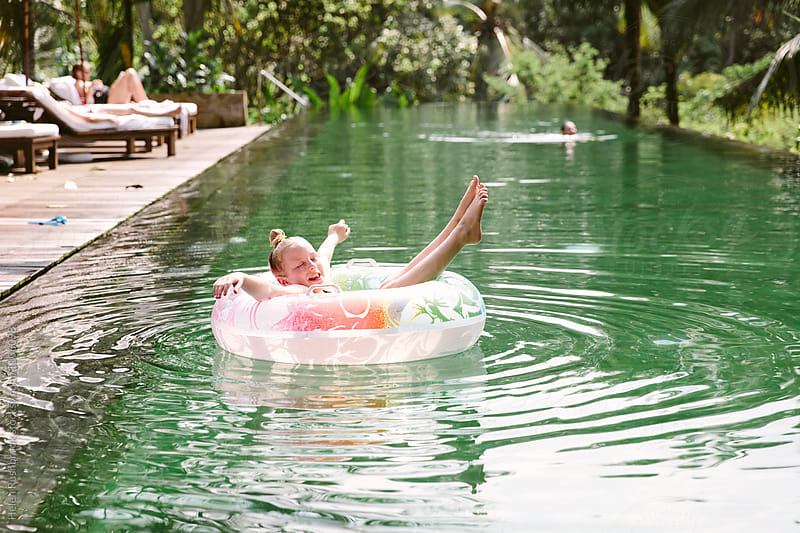 A little girl floating in a rubber ring in a swimming pool outdoors.