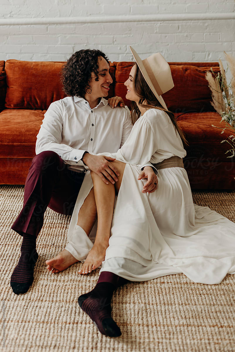 Couple hugging and smiling while sitting on the ground and leaning against velvet couch