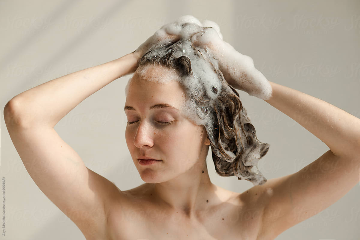 Young woman with hands touching her wet, soapy hair with shampoo foam