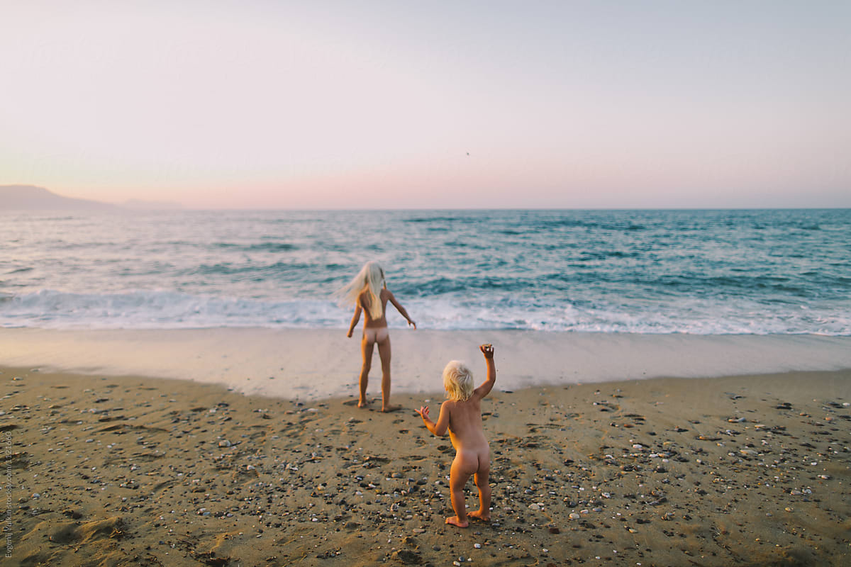Two Little Naked Sisters Playing On The Beach At Sunset 