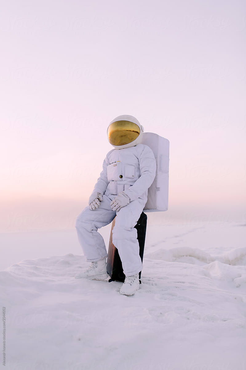Astronaut sitting on suitcase amidst snow
