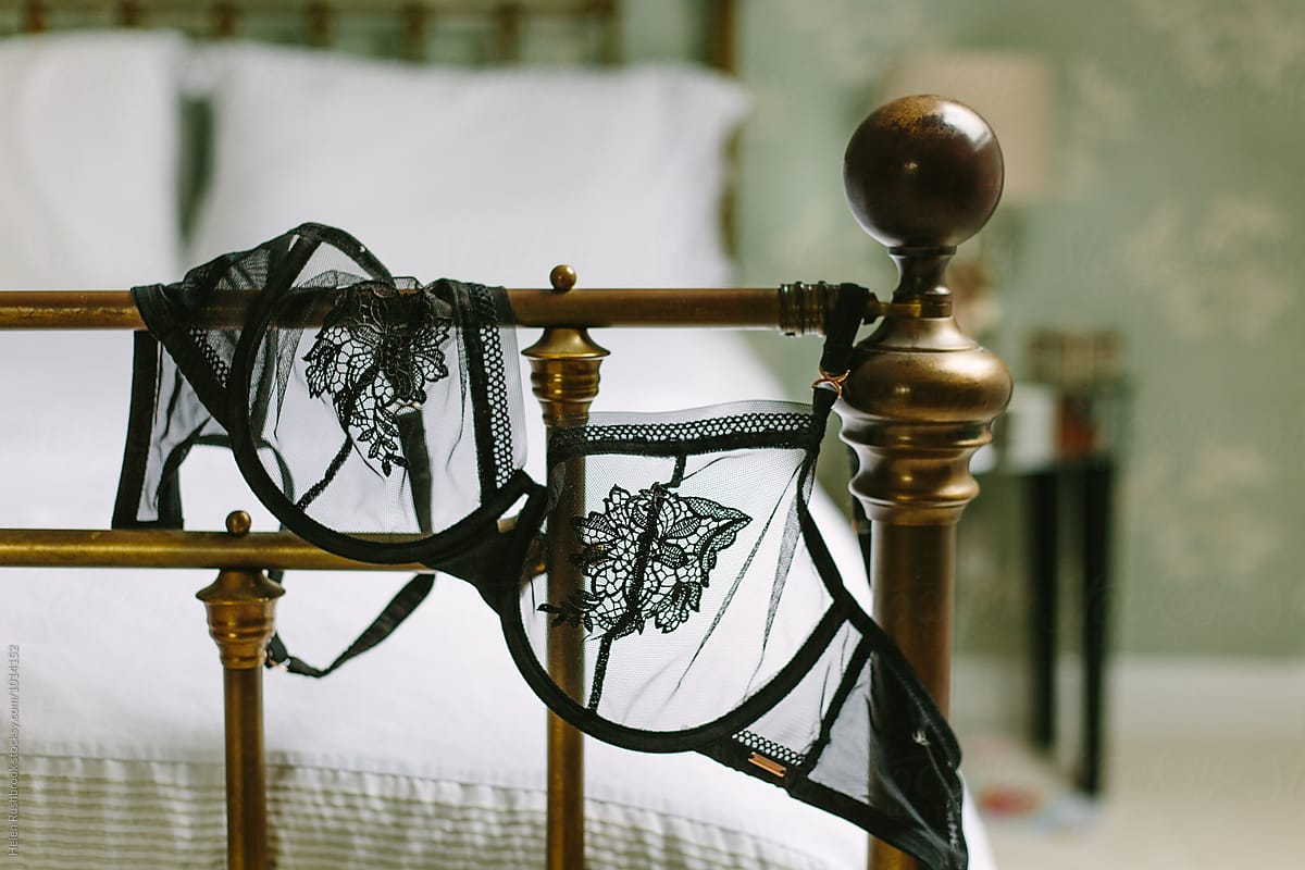 Black Mesh Bra Draped Over The End Of A Brass Bedstead by Stocksy