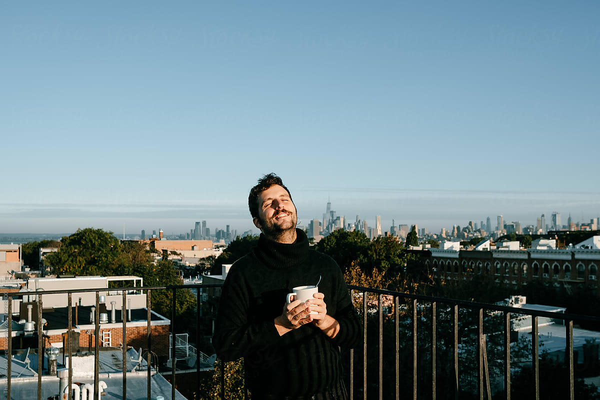 Attractive young man taking a coffee from a rooftop with the New York skyline from behind