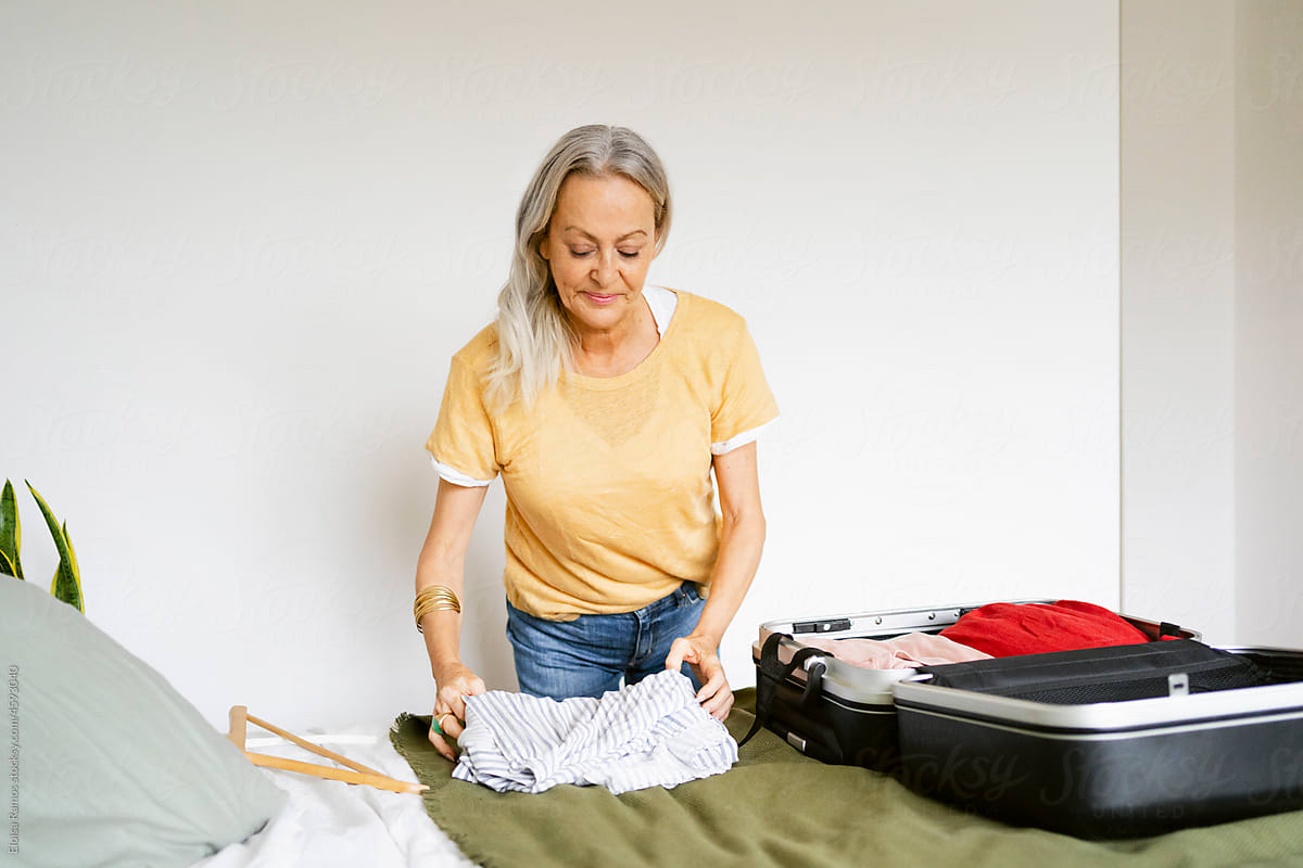 Senior casual woman preparing suitcase on bed