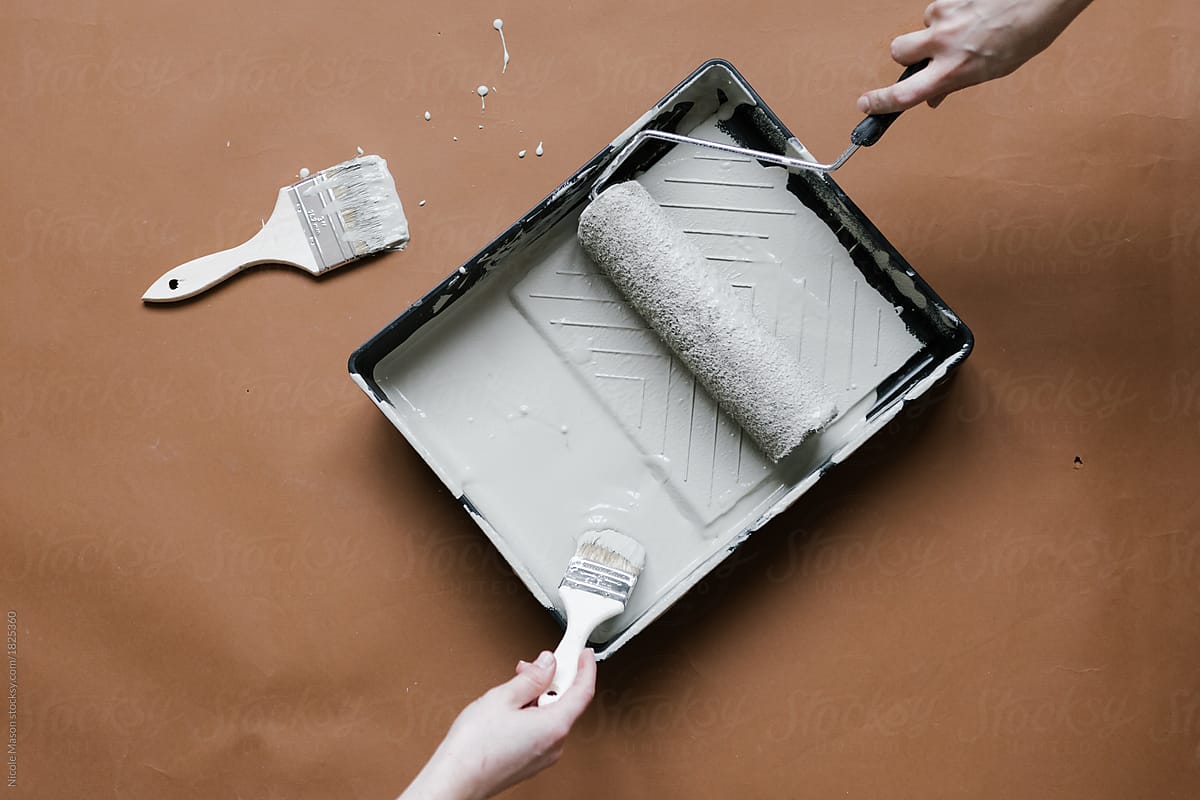 people using roller and paint brush to get paint from tray