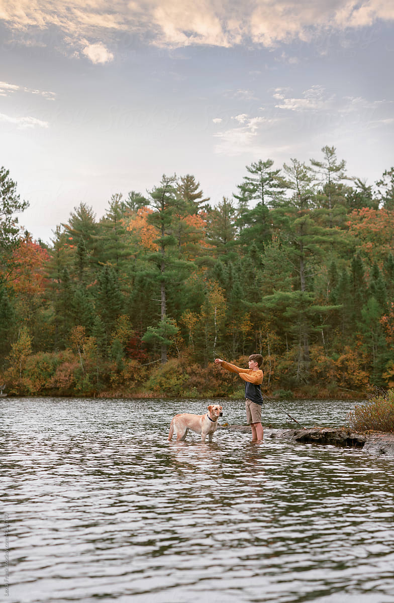 boy fishes in an autumn lake with dog