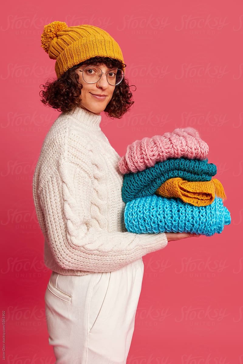 Cheerful lady with stack of knitted scarves in studio