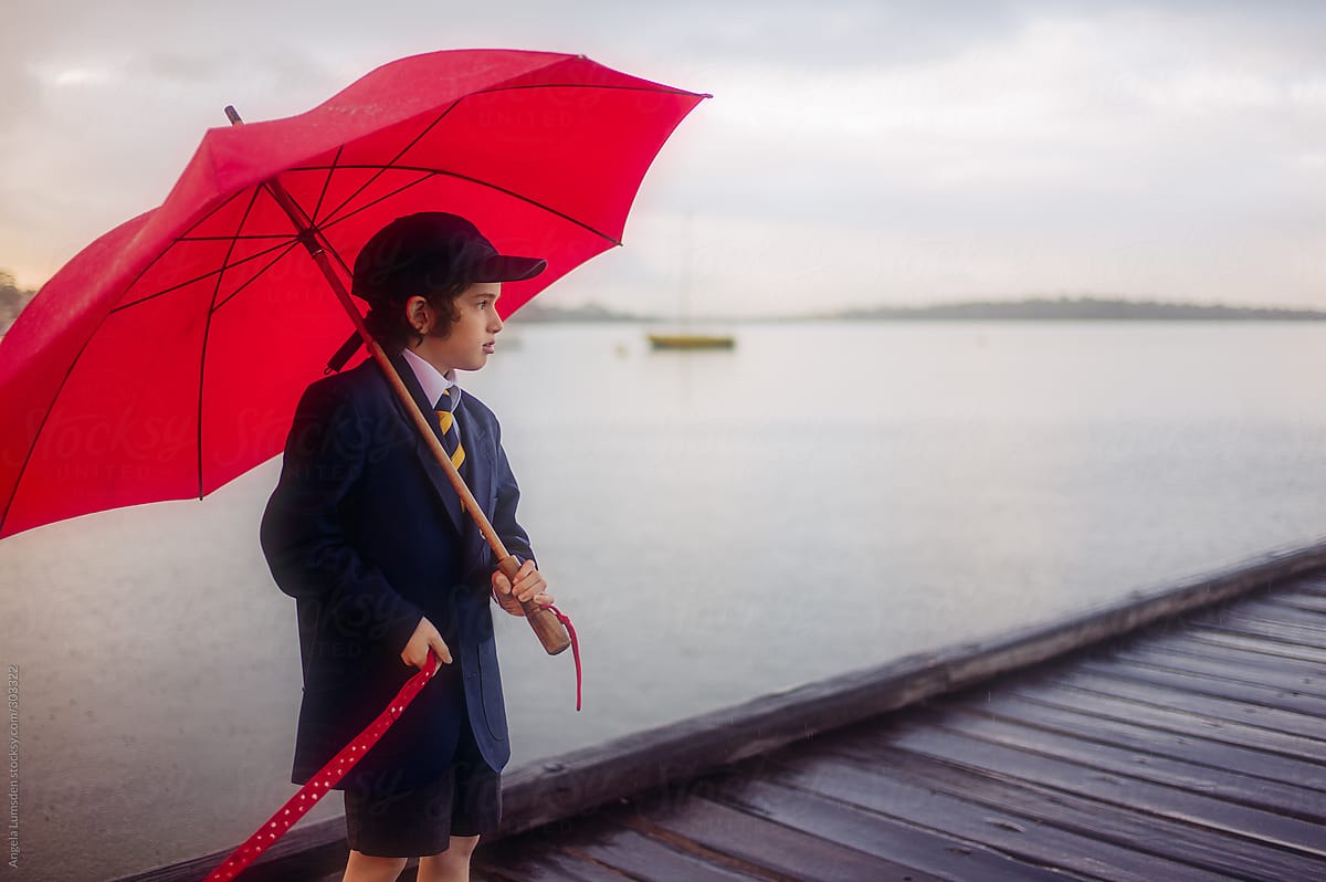 Boy with a red umbrella on a wooden dock in the rain in winter
