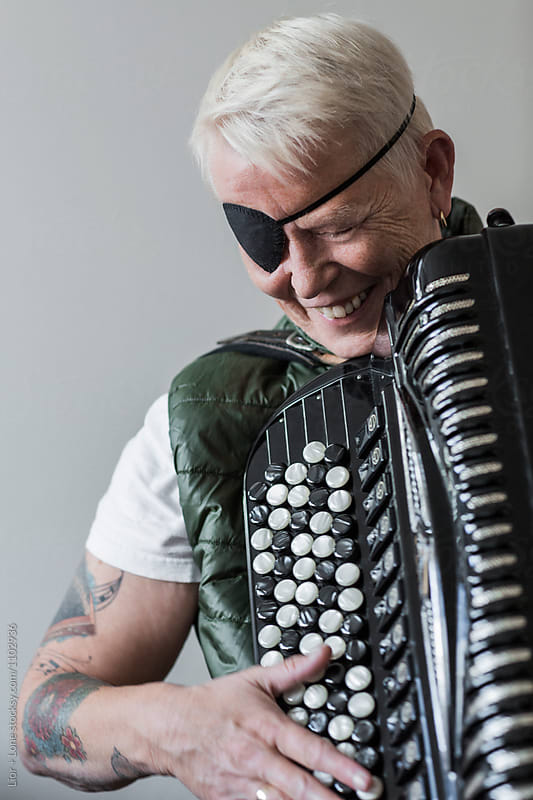 Tattooed senior woman with eye patch smiling playing accordion