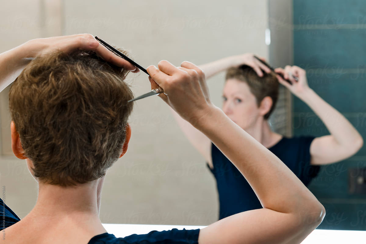 A woman gives herself a haircut at home.