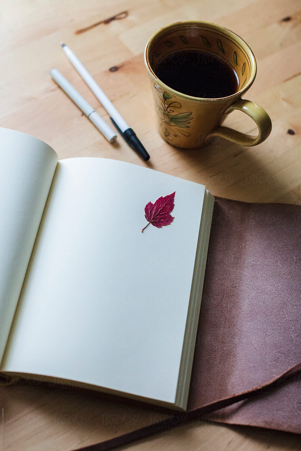 Journal page with red leaf on table next to cup of coffee