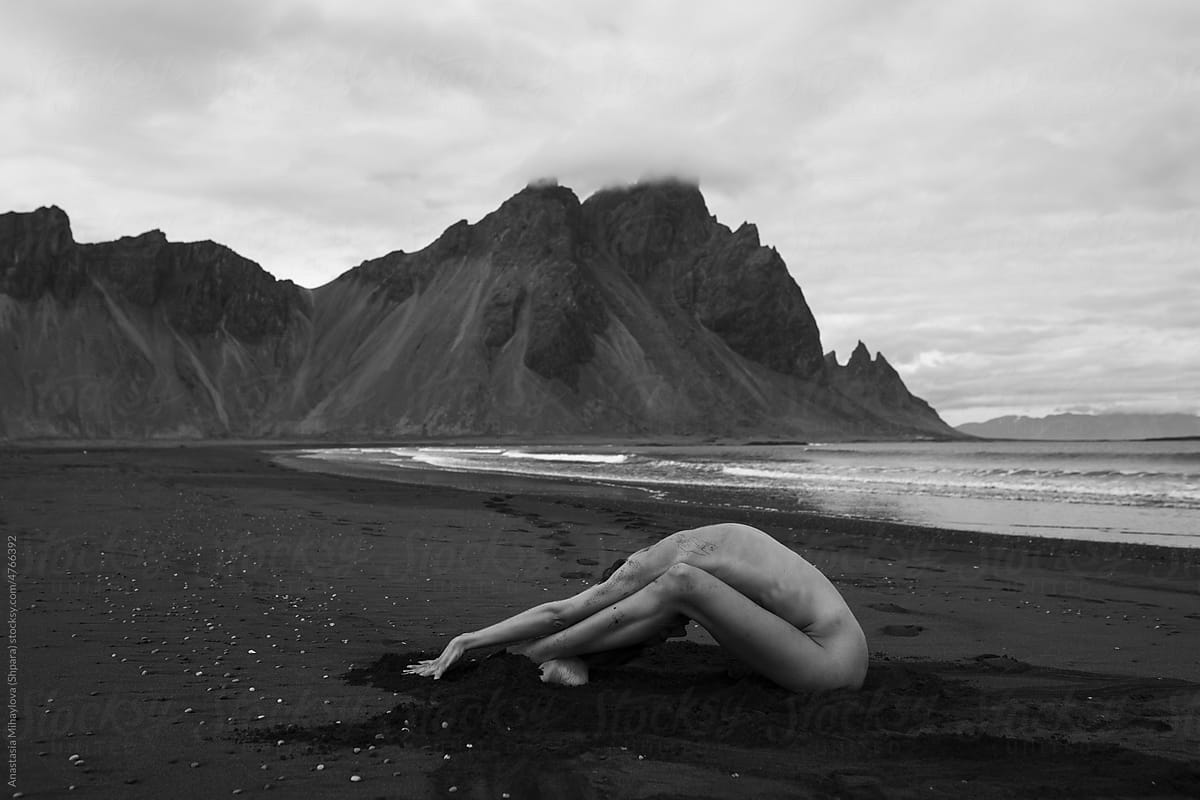 Naked woman sitting on the beach in sand near the mountains in Iceland