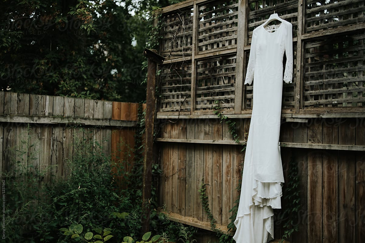 Classy minimalist wedding dress hanging on fence in overgrown ivy garden