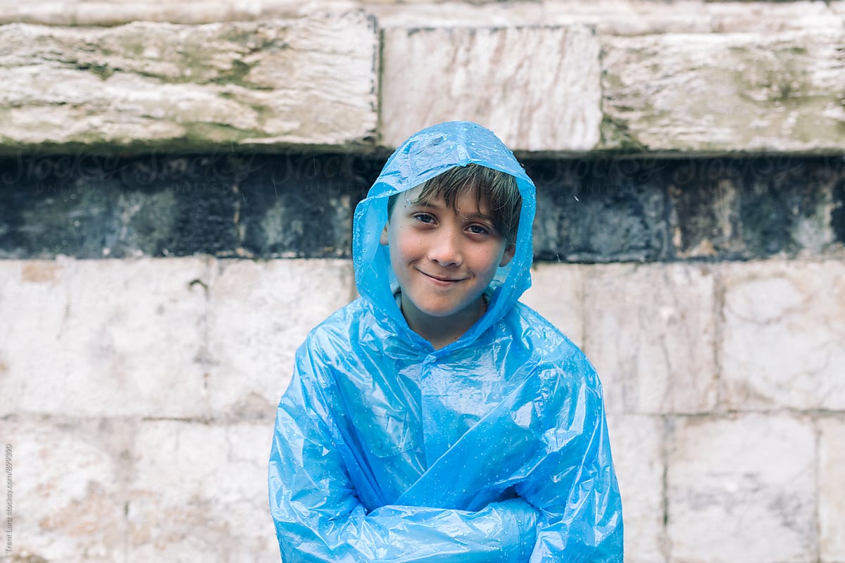 Cheerful boy wearing wet raincoat smiling in the rain