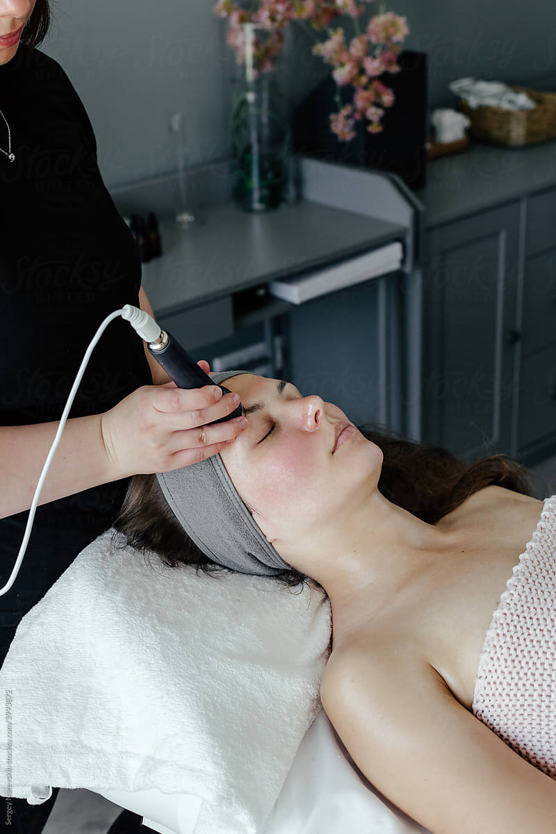 Crop female beautician doing ultrasonic massage to woman