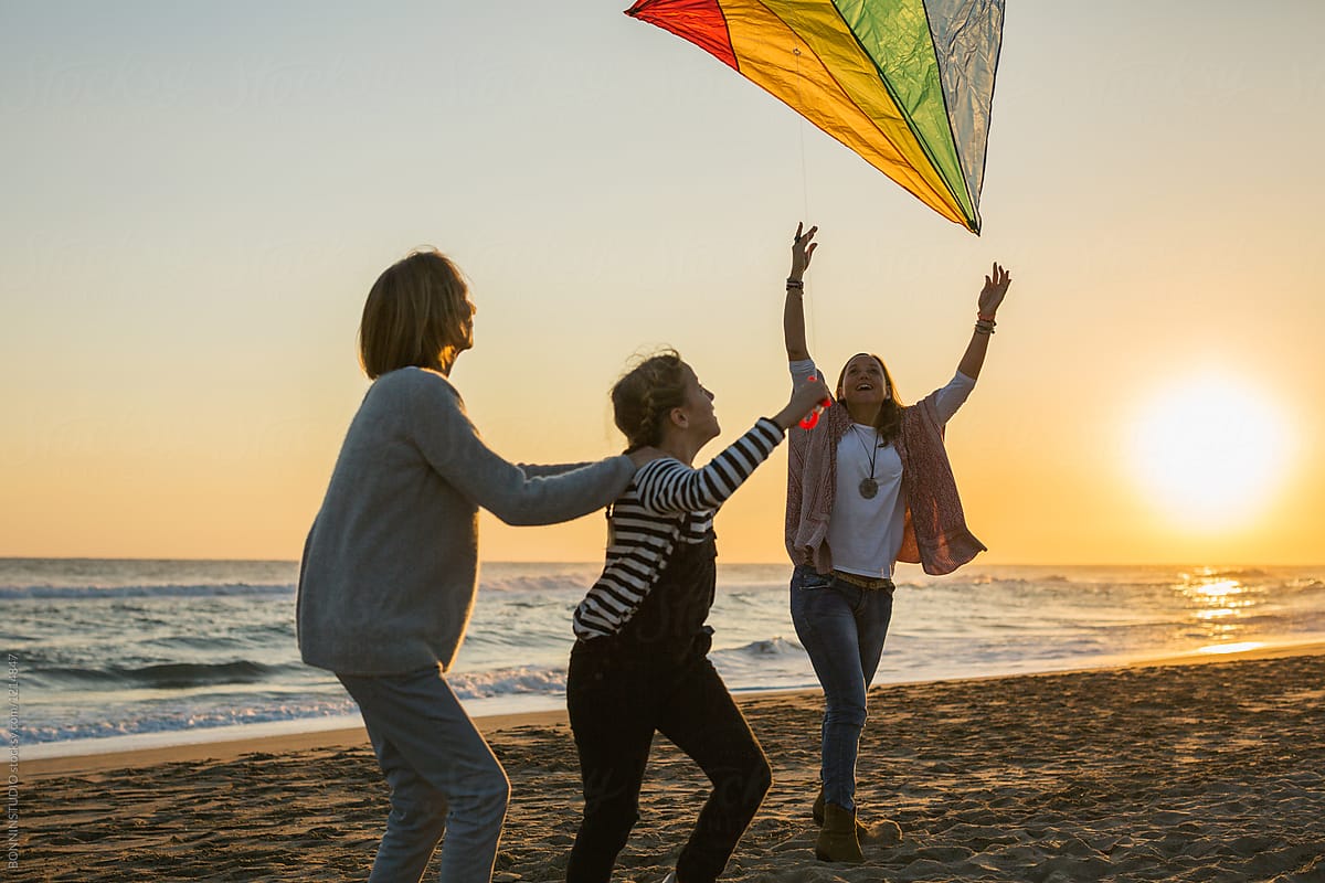 Family flying a colorful kite on the beach at sunset.