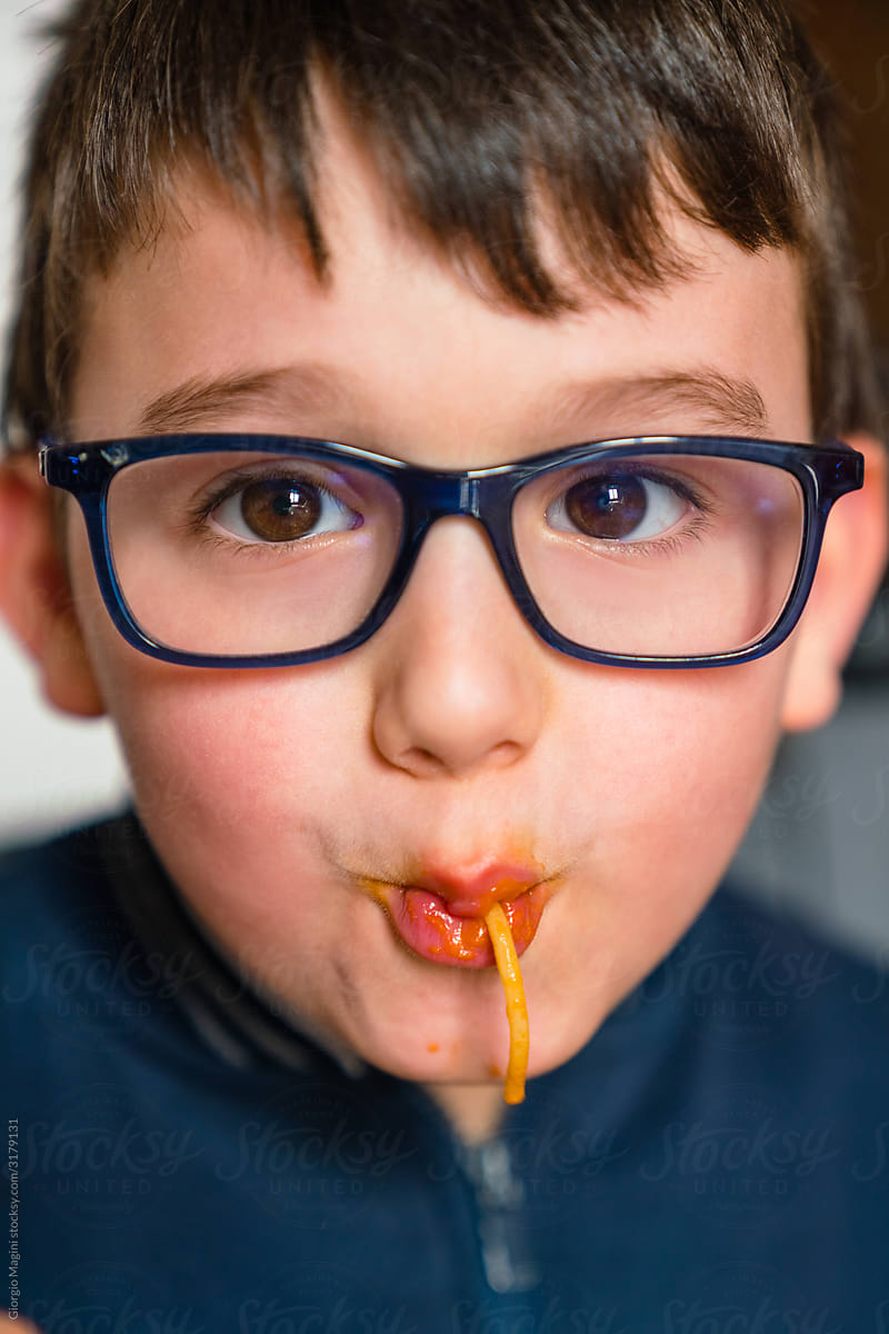 Crop funny child in eyeglasses enjoying noodles at home