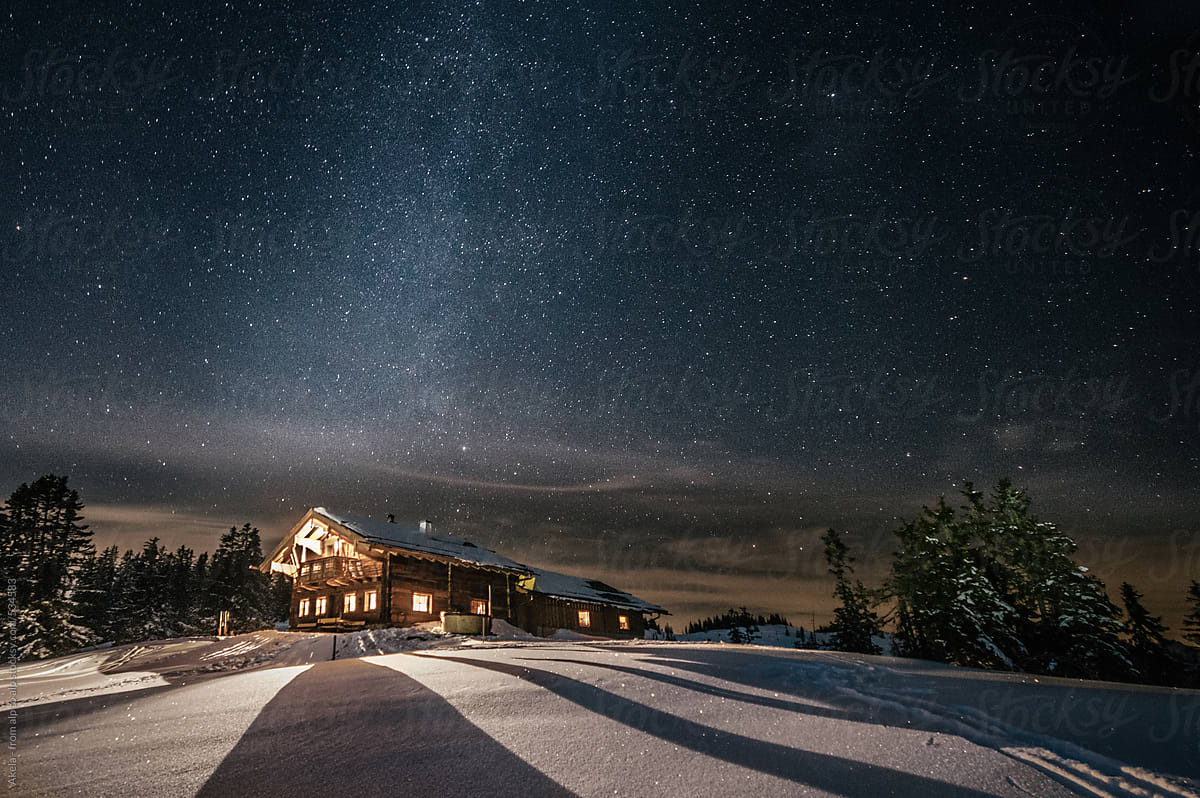 alpine cabin in snowy mountain landscape at night under the milky way