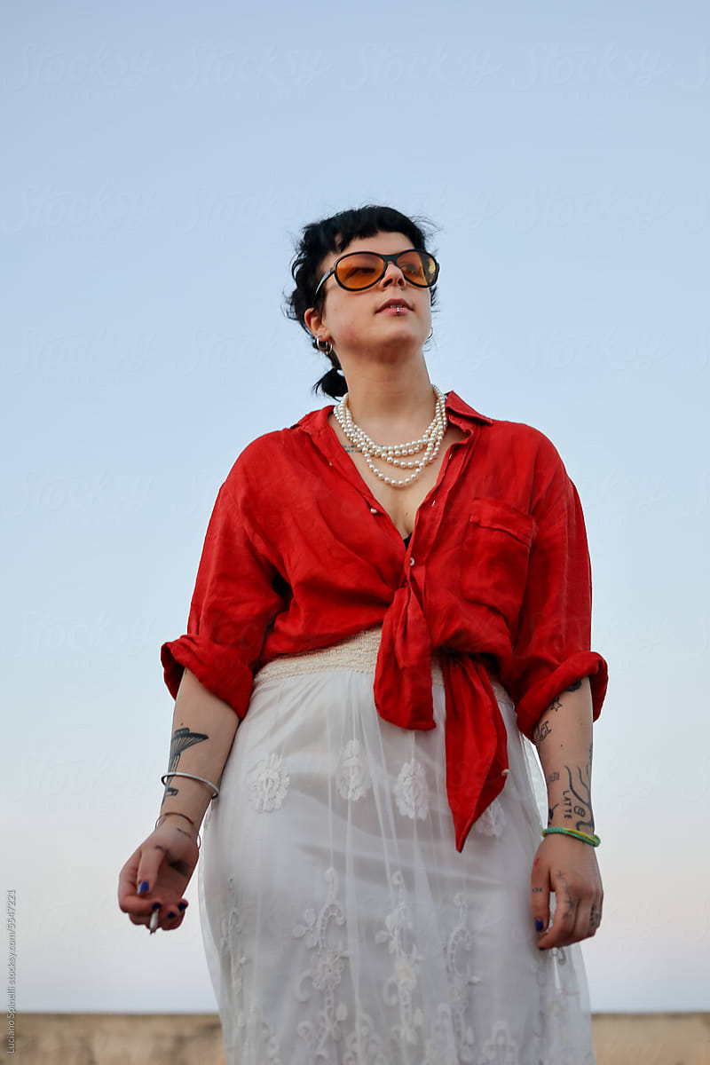 Stilysh tattooed Gen Z woman wearing sunglasses and red shirt