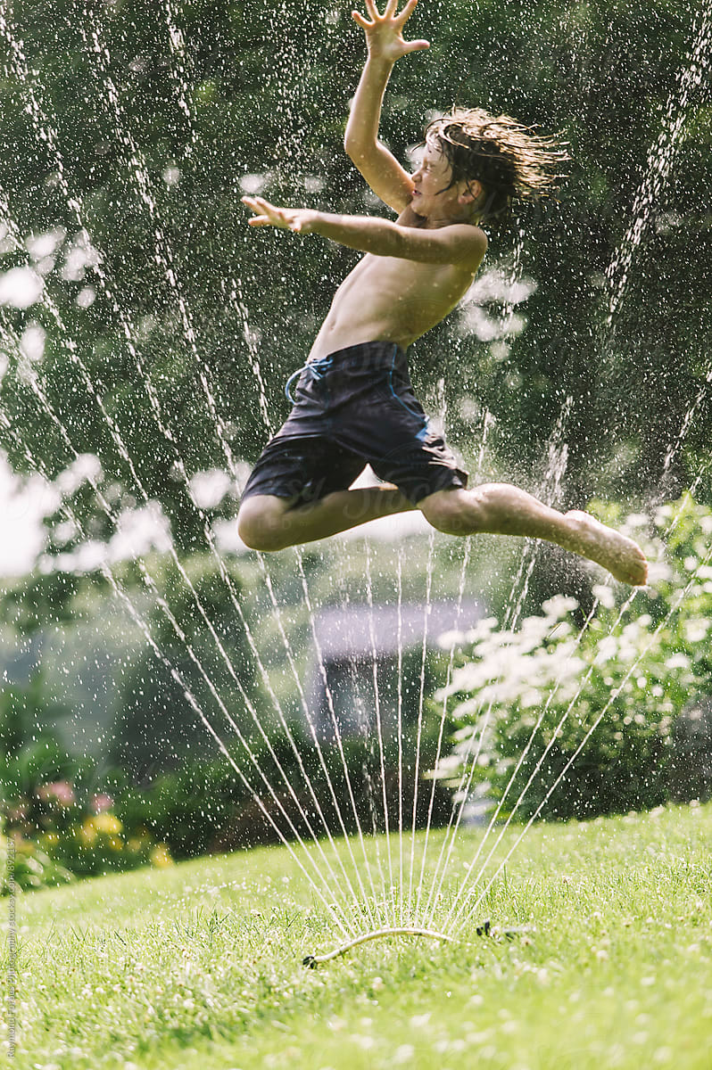 Boy Jumping Through Sprinkler in Backyard