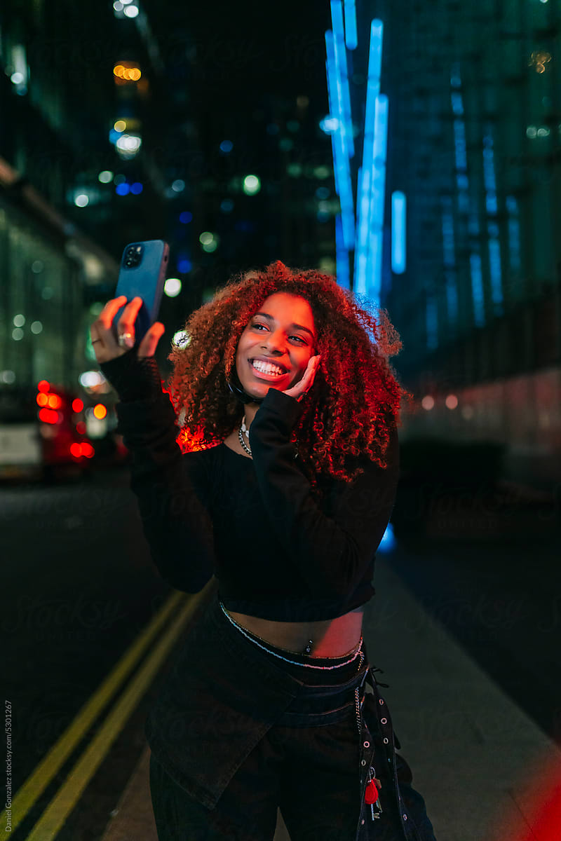 Glad black lady taking selfie on street in twilight