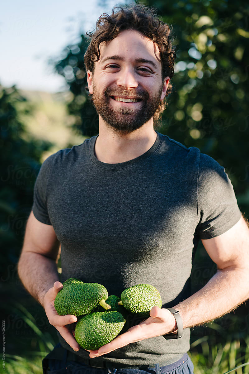 Content man with avocados in hands smiling at camera