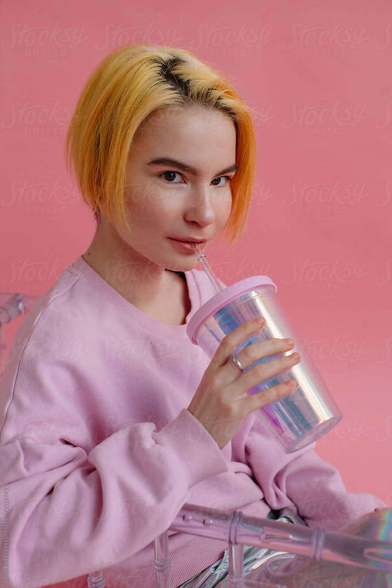 teenager with yellow hair and  holographic cup on pink background