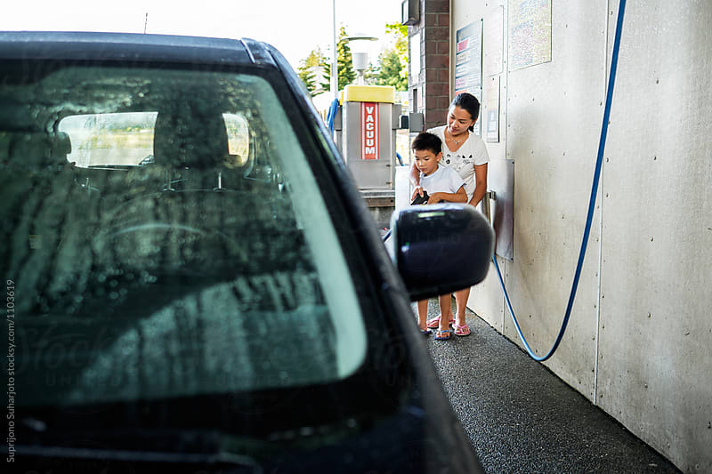 Asian woman washing a car with her kid at a car wash