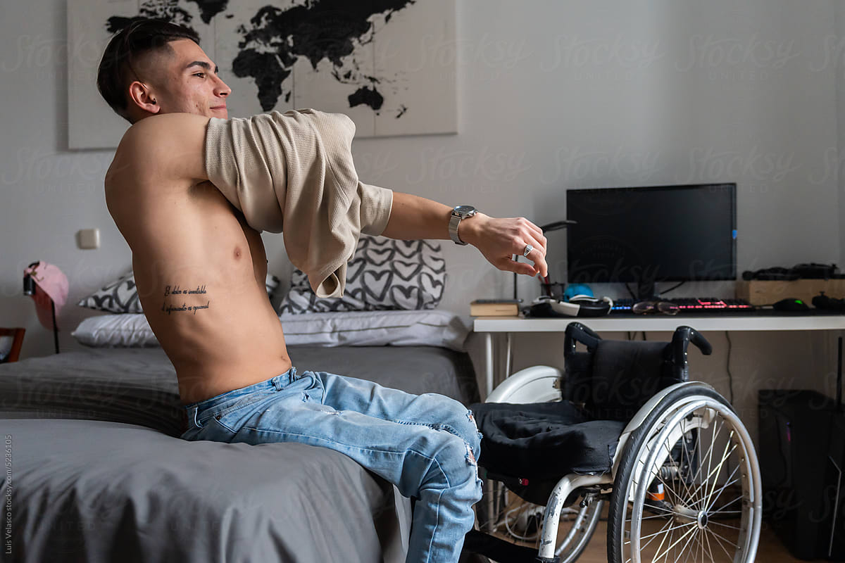 Young Man With Disability Takes Off His Shirt In His Room.