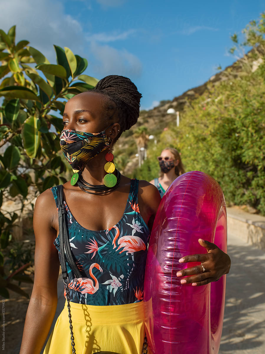 Black female in mask walking to beach in summer
