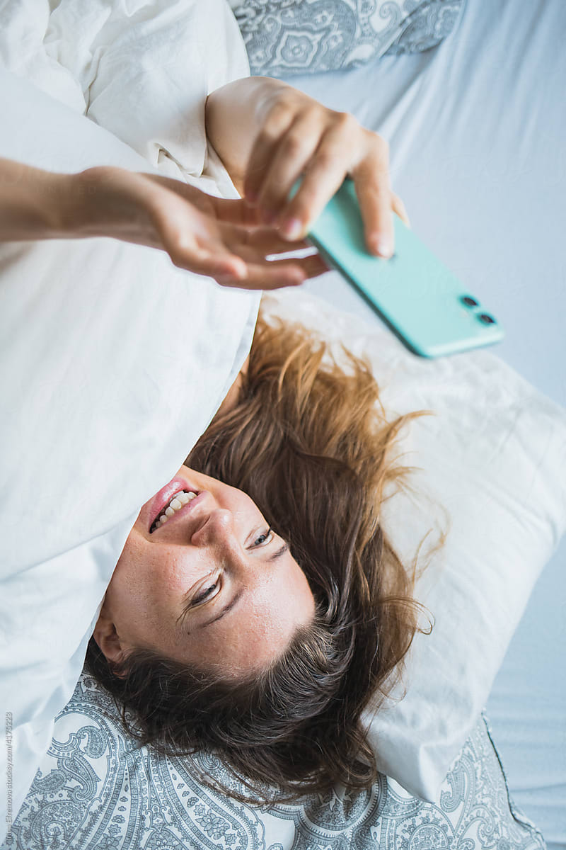 Woman in bed on the phone texting smiling