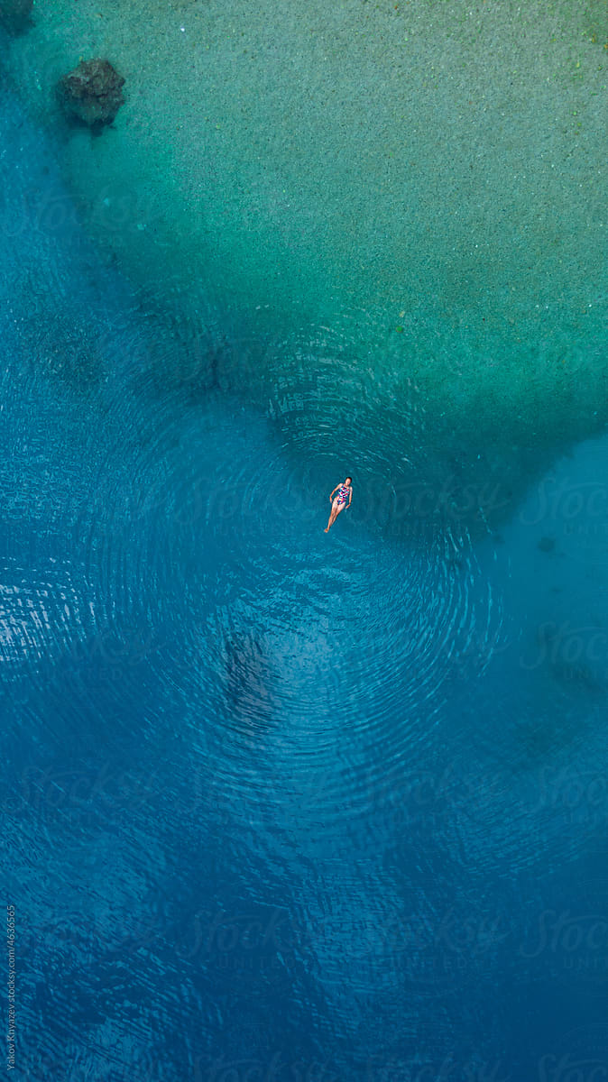 female relaxing in turquoise water, drone overhead
