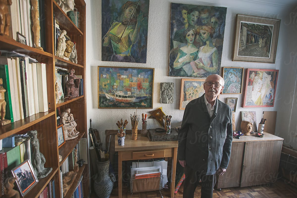Portrait of a old man standing on his studio of painting and sculpture.
